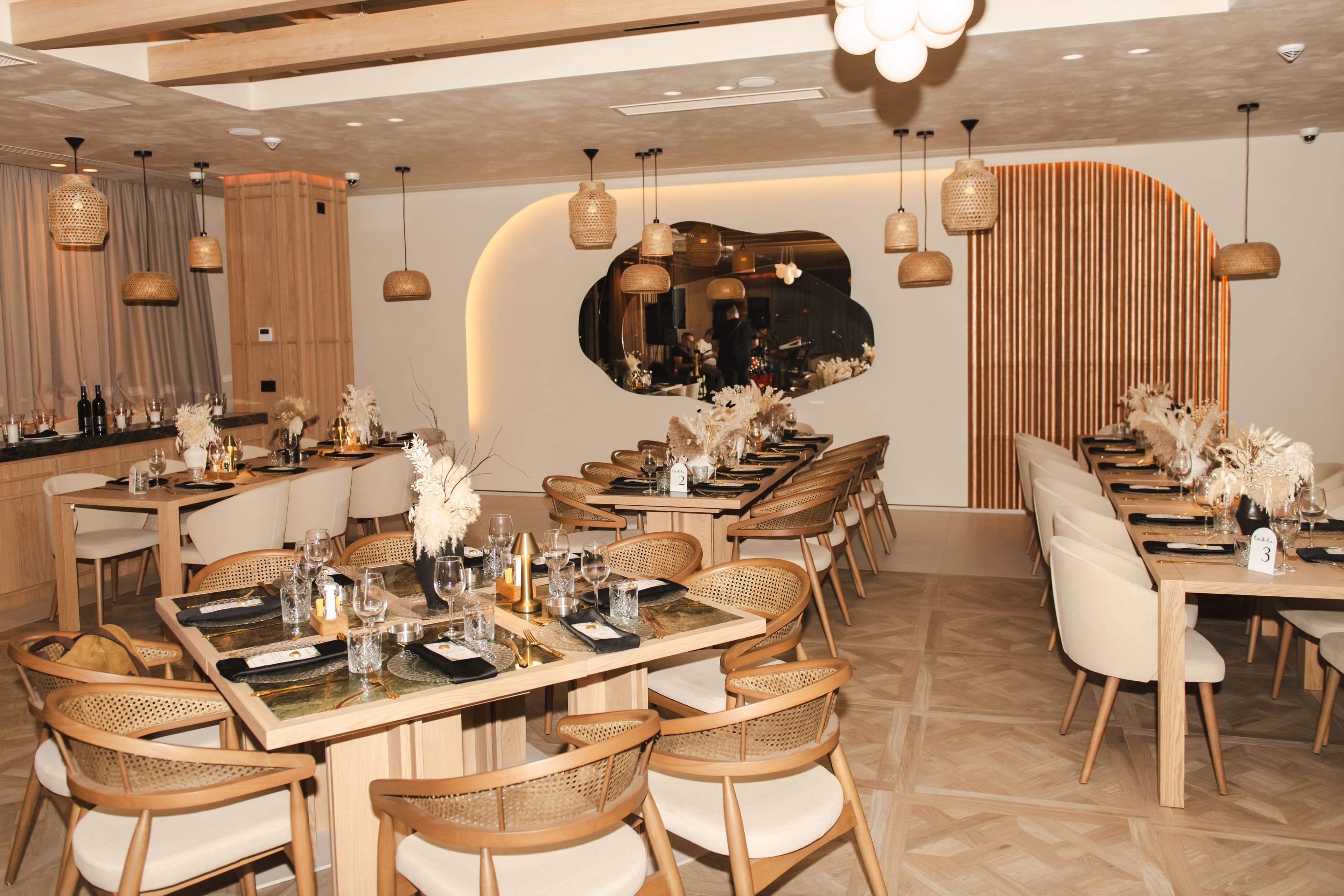 Modern restaurant interior featuring set wooden tables, woven pendant lights, and neutral decor.