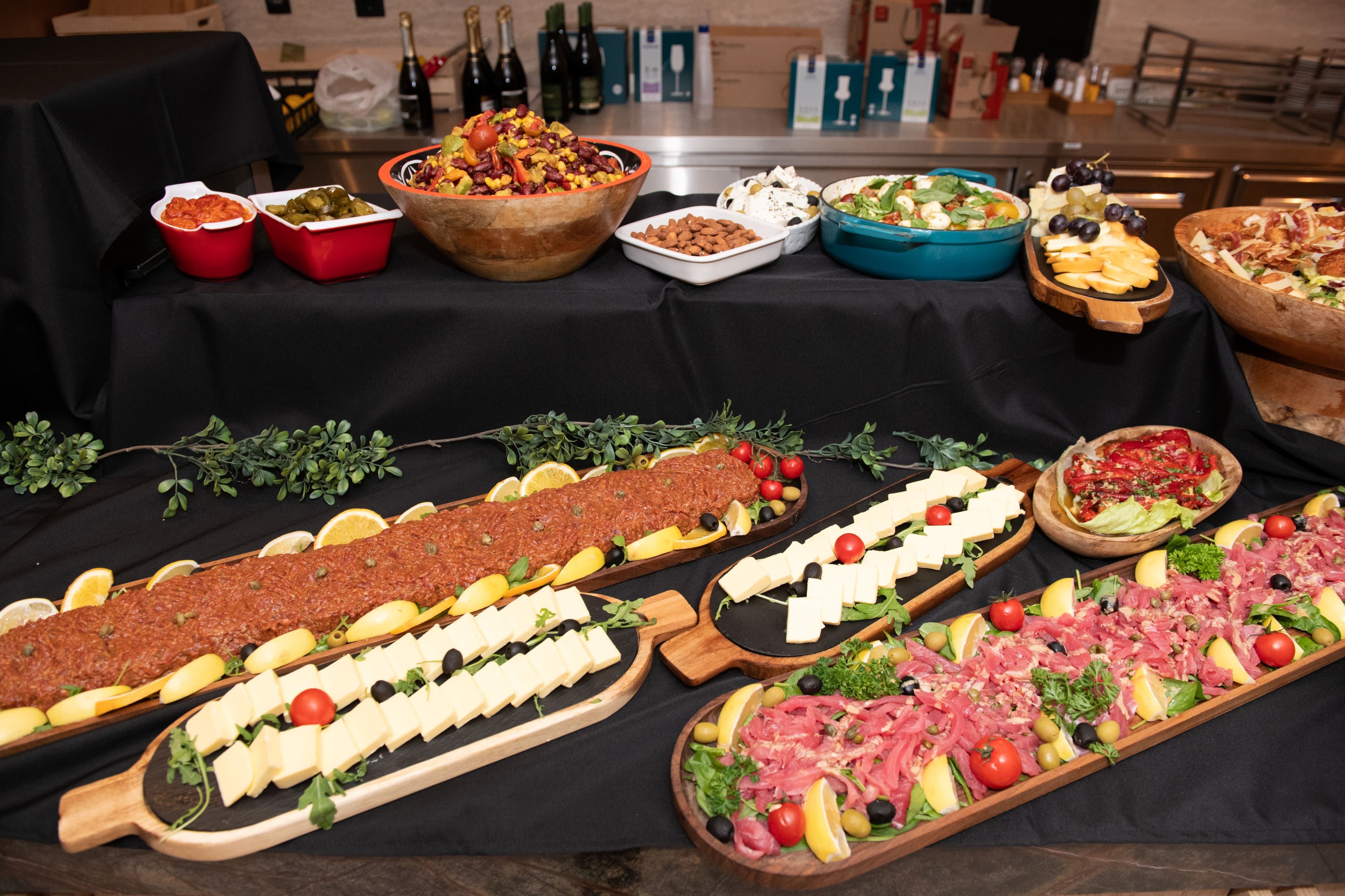 Gourmet appetizer spread featuring meat carpaccio, cheese platters, and salads on a black tablecloth.