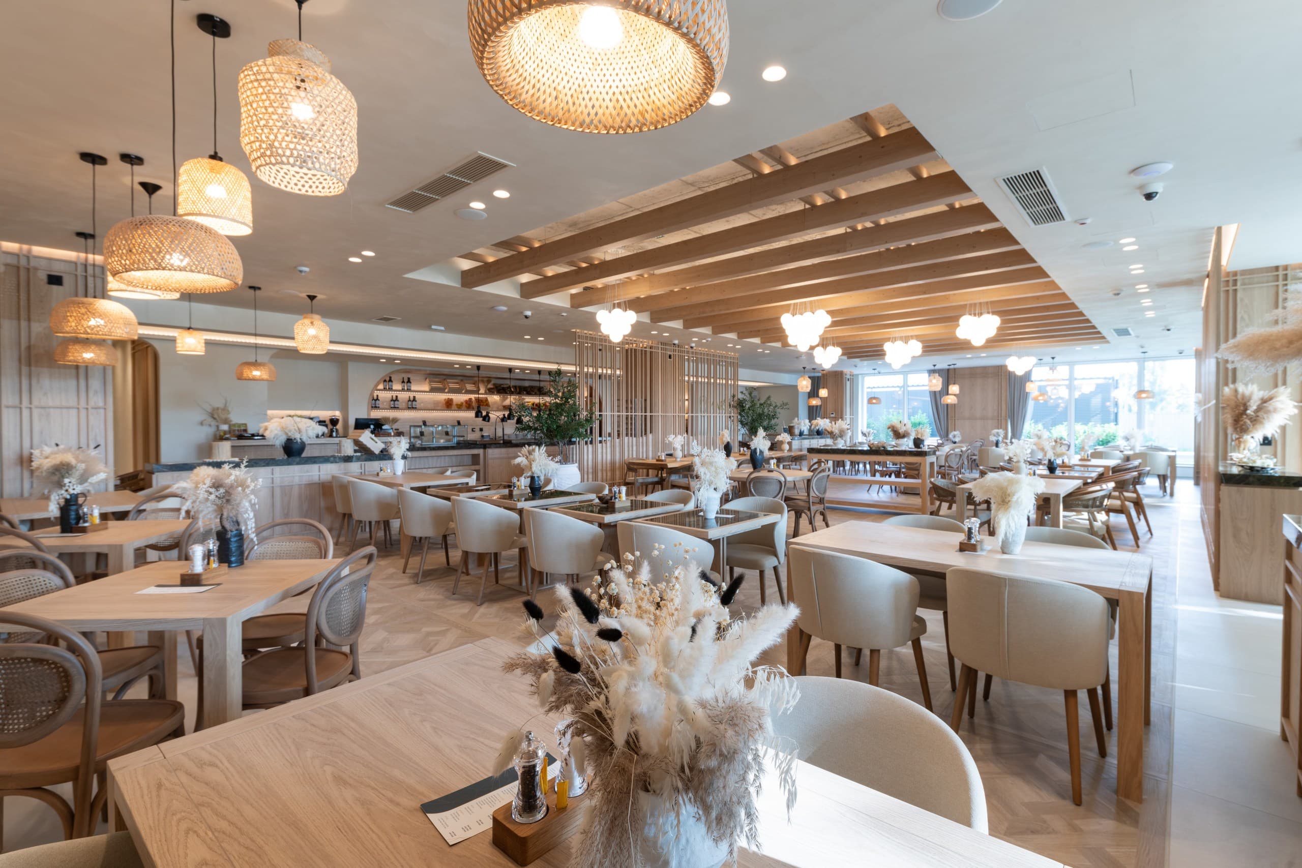 Bright, modern restaurant interior with light wood tables, cream chairs, and woven wicker pendant lights.